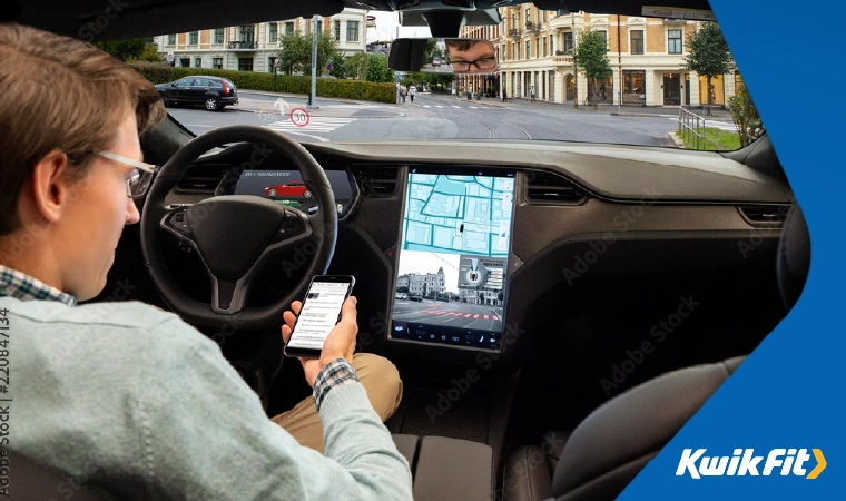 Person using phone whilst sitting in the drivers seat of a self driving car.