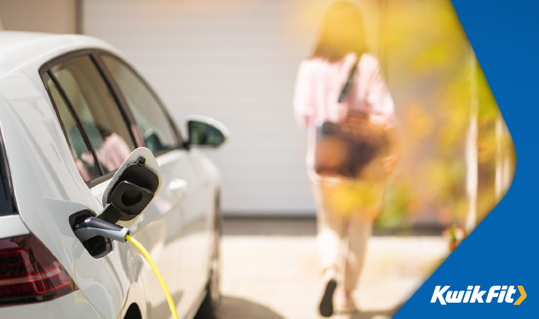 Person walking towards house whilst white car charges using electric car charging cable.