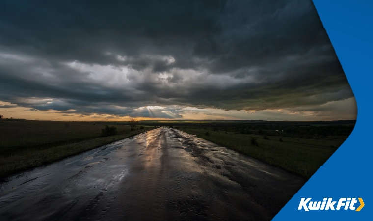 A wet, pothole-filled road under dark, stormy clouds.