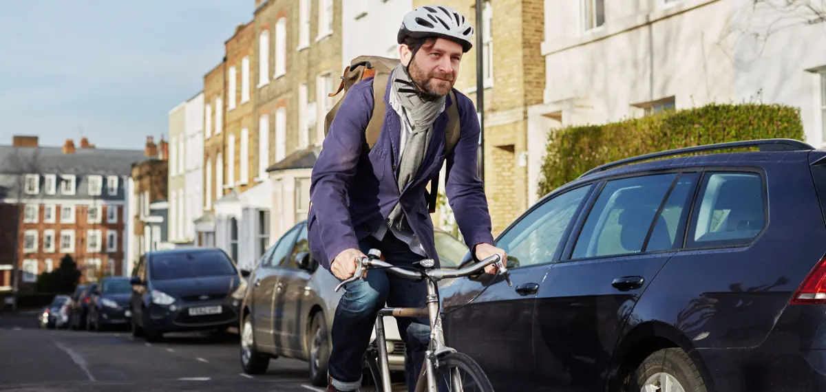 Cyclist riding bike on a road with parked cars