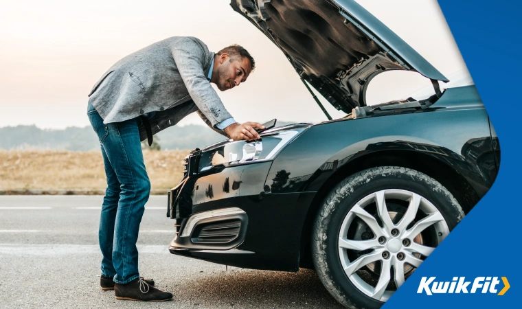 Man in smart clothes attempting to find an engine fault at the side of a rural road.