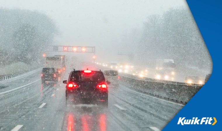 Cars driving through heavy snow on a motorway, leaving lots of room between each other.