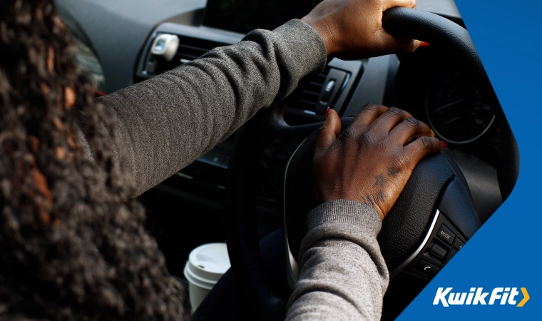 A person pressing down on their horn with their right hand whilst holding the steering wheel with their left hand.