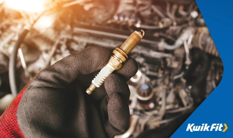 Technician holding a spark plug with a red and black glove on.