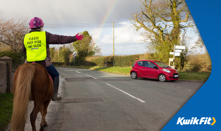 A rider on horseback signals to a car at a junction.