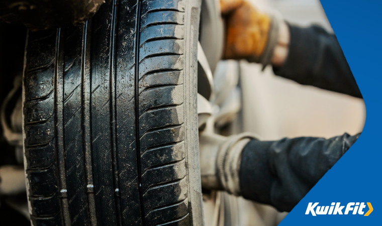 Technician with gloves on removing a muddy and wet wheel from a car.