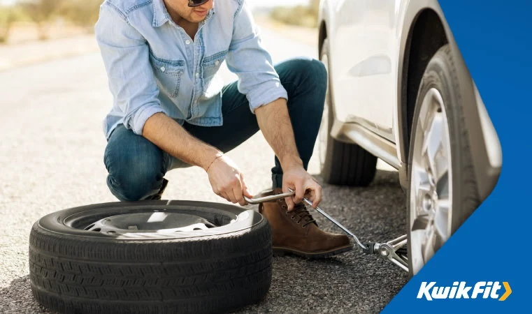 Man replacing a punctured car tyre on the side of a road.