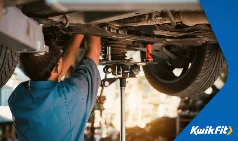 A mechanic works on the suspension of a car which is lifted above him.