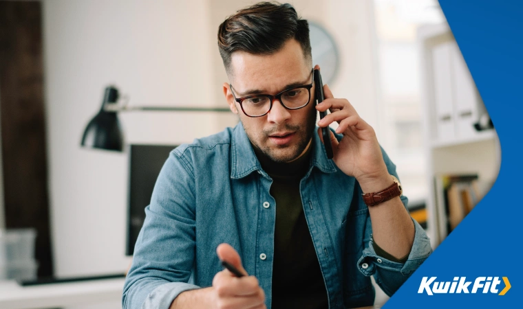 Man sitting at a desk on a phone call with a pen in one hand.