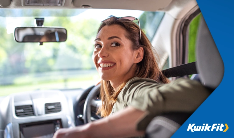 Woman with sunglasses on top of her head in the drivers seat of a car turning around smiling.