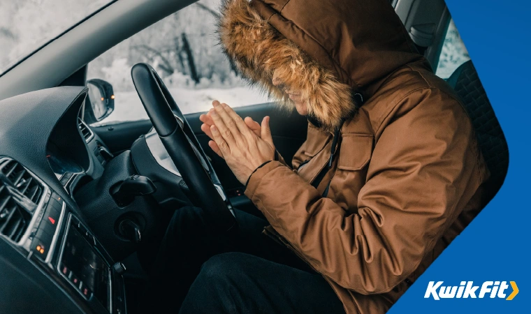 A person warming up by their car heater in a big coat.