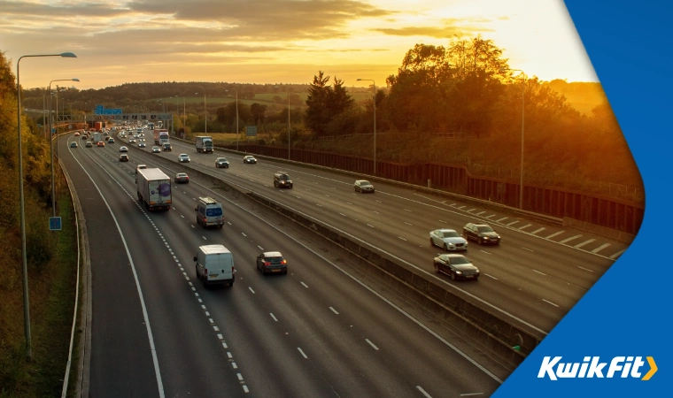 The sunsetting on a busy motorway with cars driving on either side surrounded by greenery.