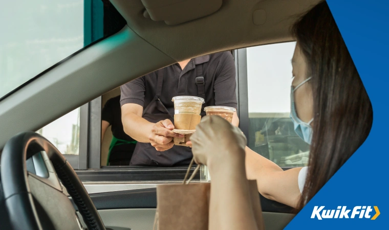 Person collecting their food and drinks in their car at a drive-thru window.