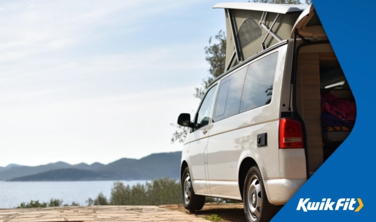 Pop-top VW Transporter minivan camper parked on hard standing spot at a campsite.