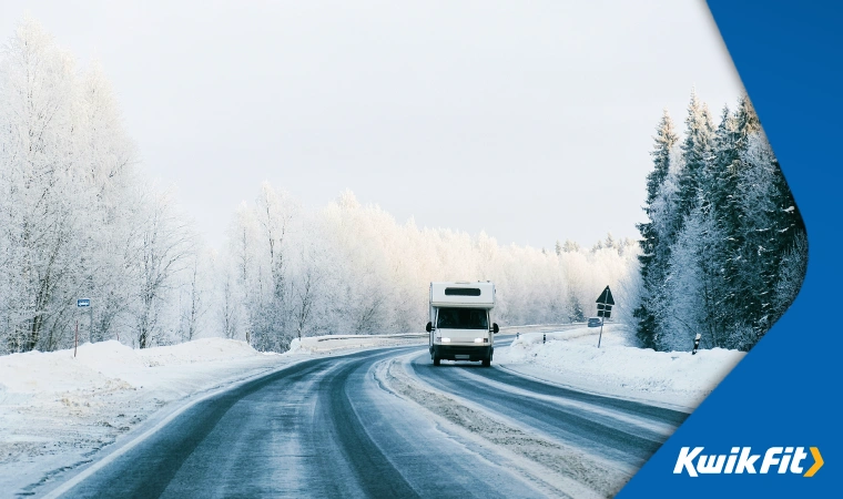 a motorhome drives carefully along a frozen road  the trees alongside are all covered in snow in front of an almost-white sky.